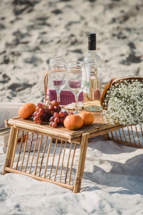 Free Outdoor picnic setup on a sandy beach with wine, grapes, and flowers. Stock Photo