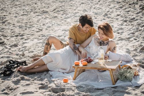 Free Young couple enjoying a relaxed picnic on a sunny beach, sharing laughter and affection. Stock Photo