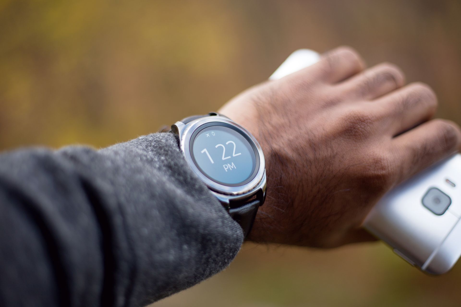 Close-up of a smartwatch on a man's wrist holding a mobile phone in natural light.