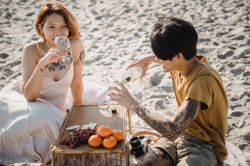 Free A couple enjoys a wine picnic on the beach with fresh fruits under the sun. Stock Photo