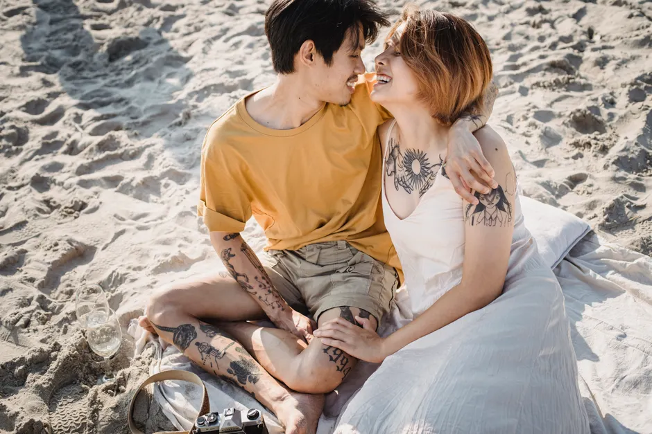 Couple assis sur le sable, bras et épaules couverts de tatouages figuratifs