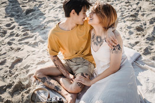 Affectionate couple with tattoos enjoying a sunny day at the beach, embracing on the sand.