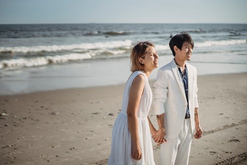 Man and Woman in White Clothes Walking on Beach