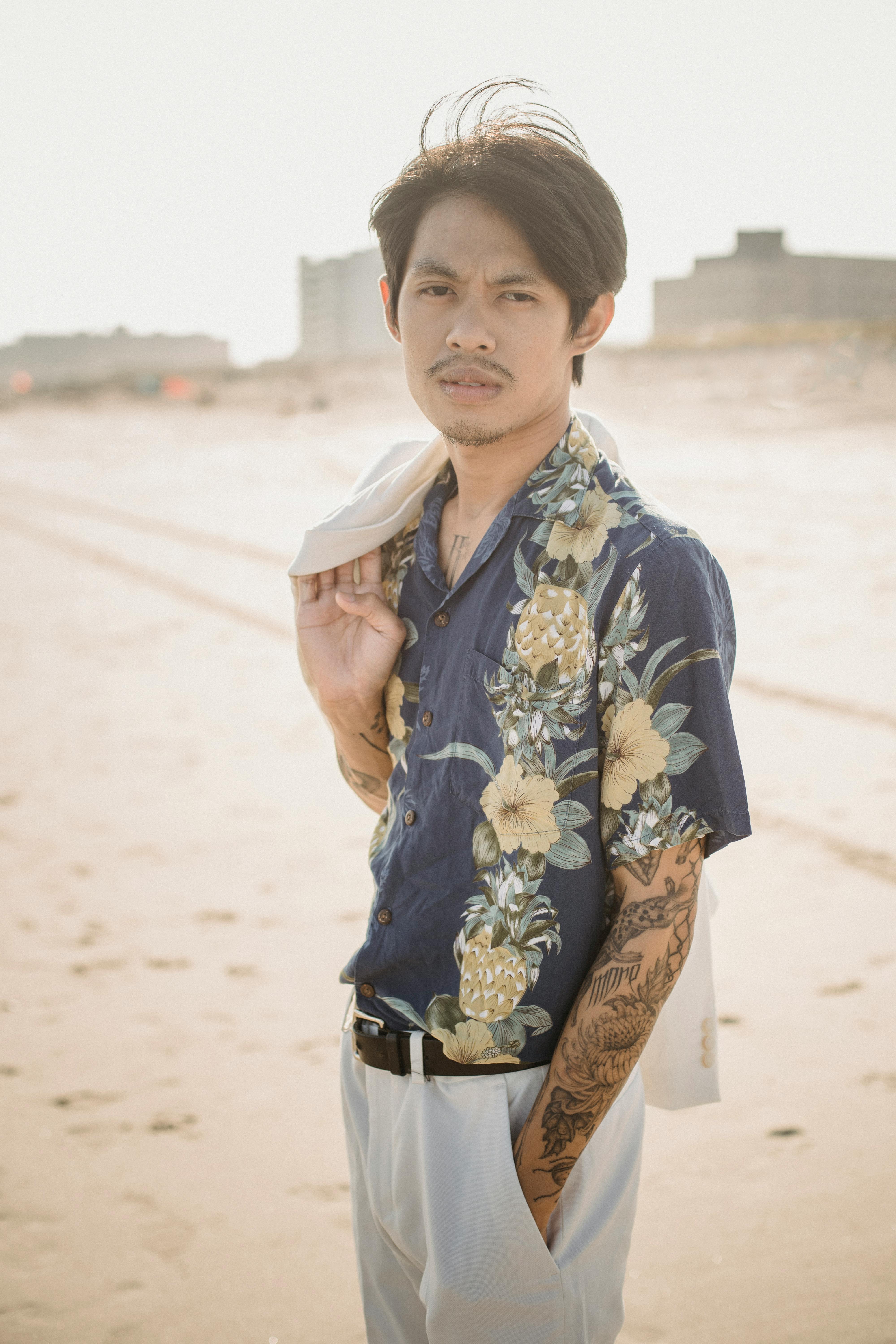 一位时尚男子穿着花卉衬衫，在阳光明媚的海滩上自信地摆出姿势