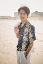 一位时尚男子穿着花卉衬衫，在阳光明媚的海滩上自信地摆出姿势