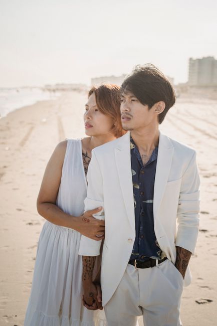 A couple in elegant attire shares a tender moment on a sunlit beach, evoking romance and tranquility.