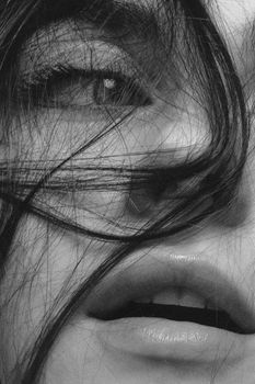 Artistic close-up portrait of a woman's face with hair over her eye and lips.