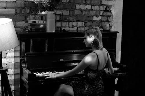 Black and white side view of focused female playing piano while rehearsing in room at brick wall near vase with flowers