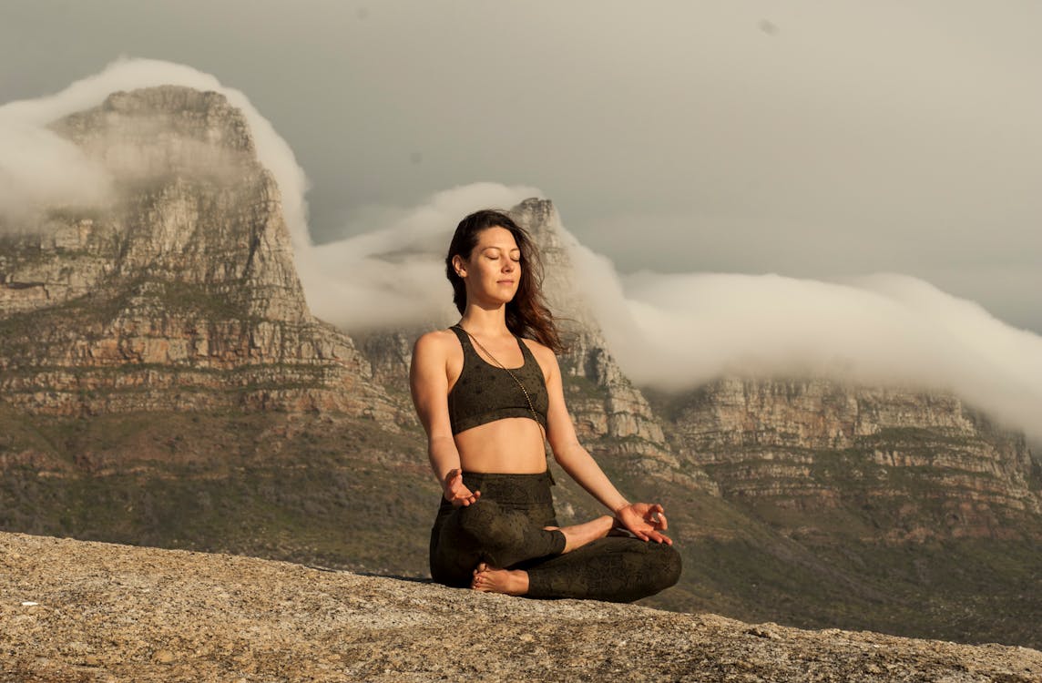 Free Woman in Black Sports Bra and Black Pants Sitting on Rock  Stock Photo