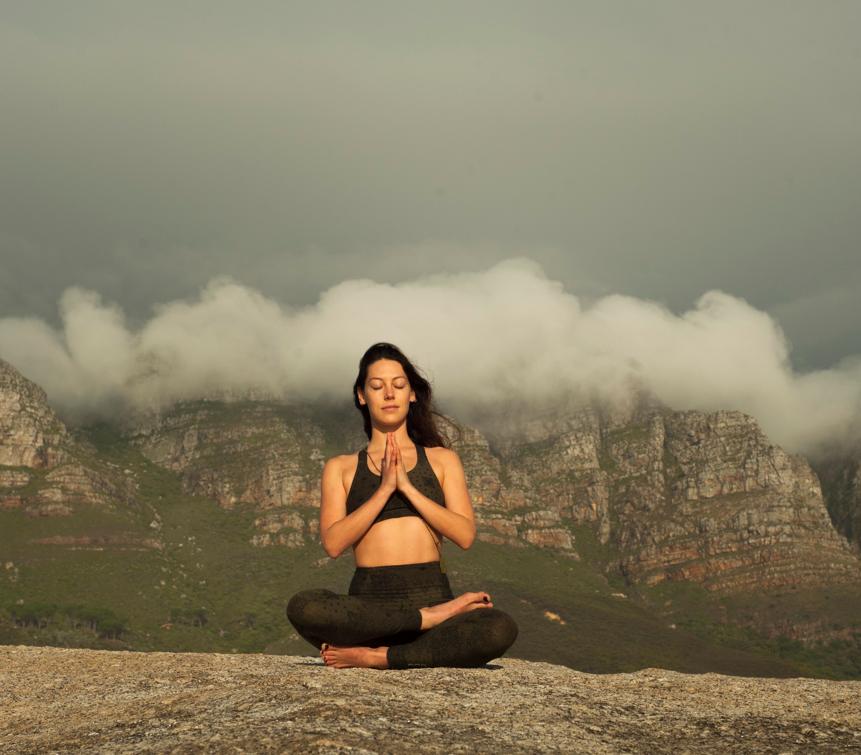 A woman practices yoga meditation outdoors in a serene mountain setting, promoting relaxation and wellness.