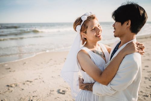 Free A couple in wedding attire embraces on a sunny beach, exuding love and romance. Stock Photo