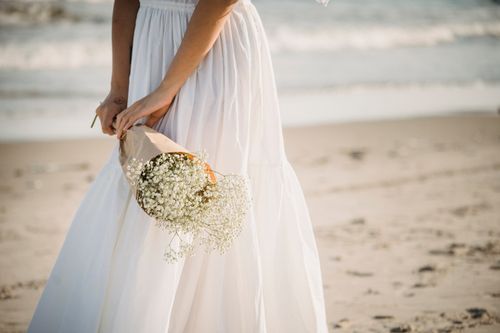 Free Bride in a white dress holding flowers by the seashore on a sunny day. Stock Photo