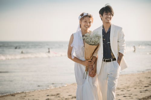 Man in White Suit and Woman in White Dress Standing on the Beach