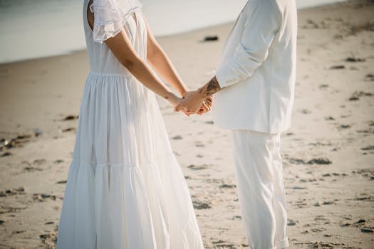 A couple in wedding attire holding hands on a sandy beach, symbolizing romance and togetherness.