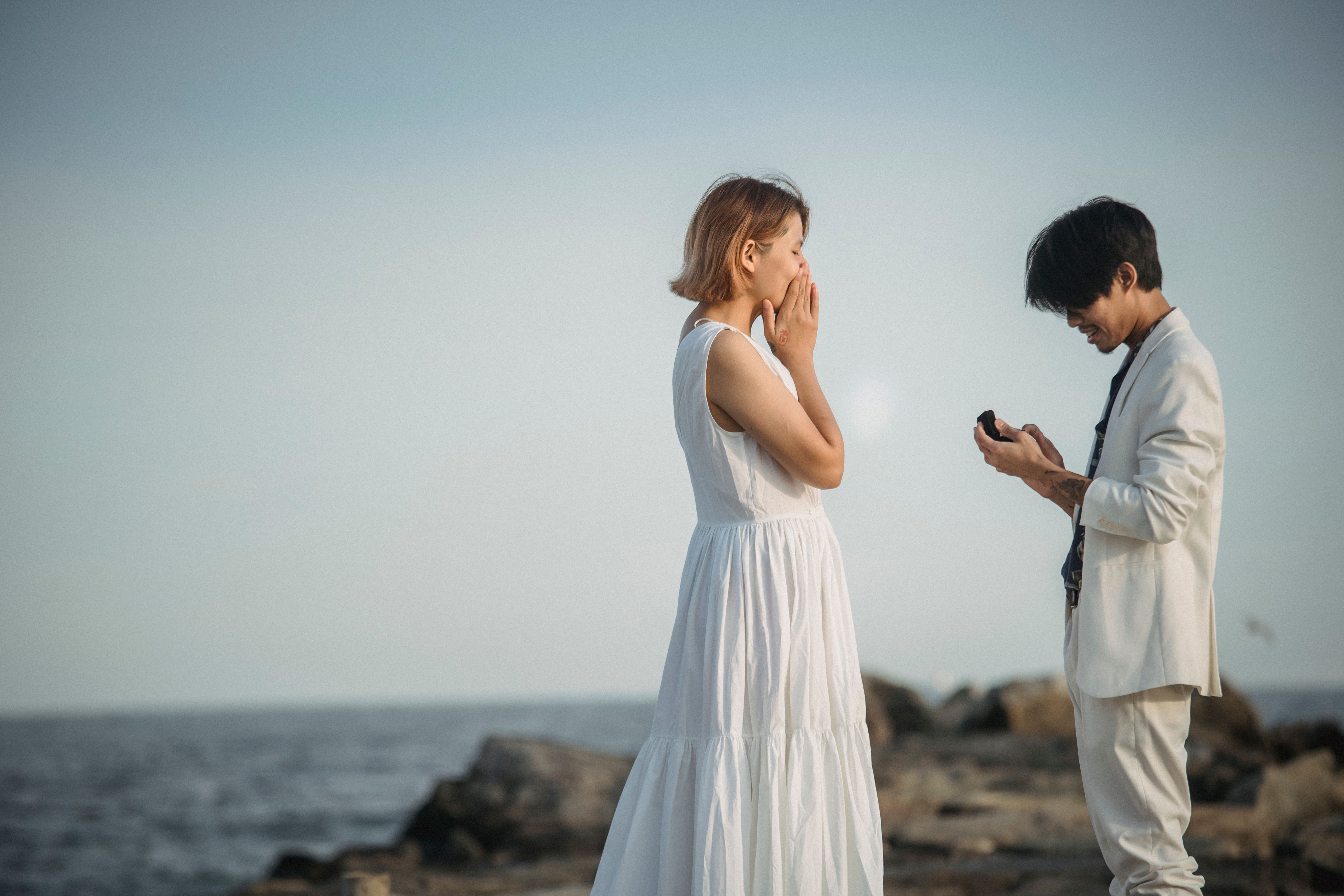 A man proposing marriage to a woman on a rocky beach at sunset.