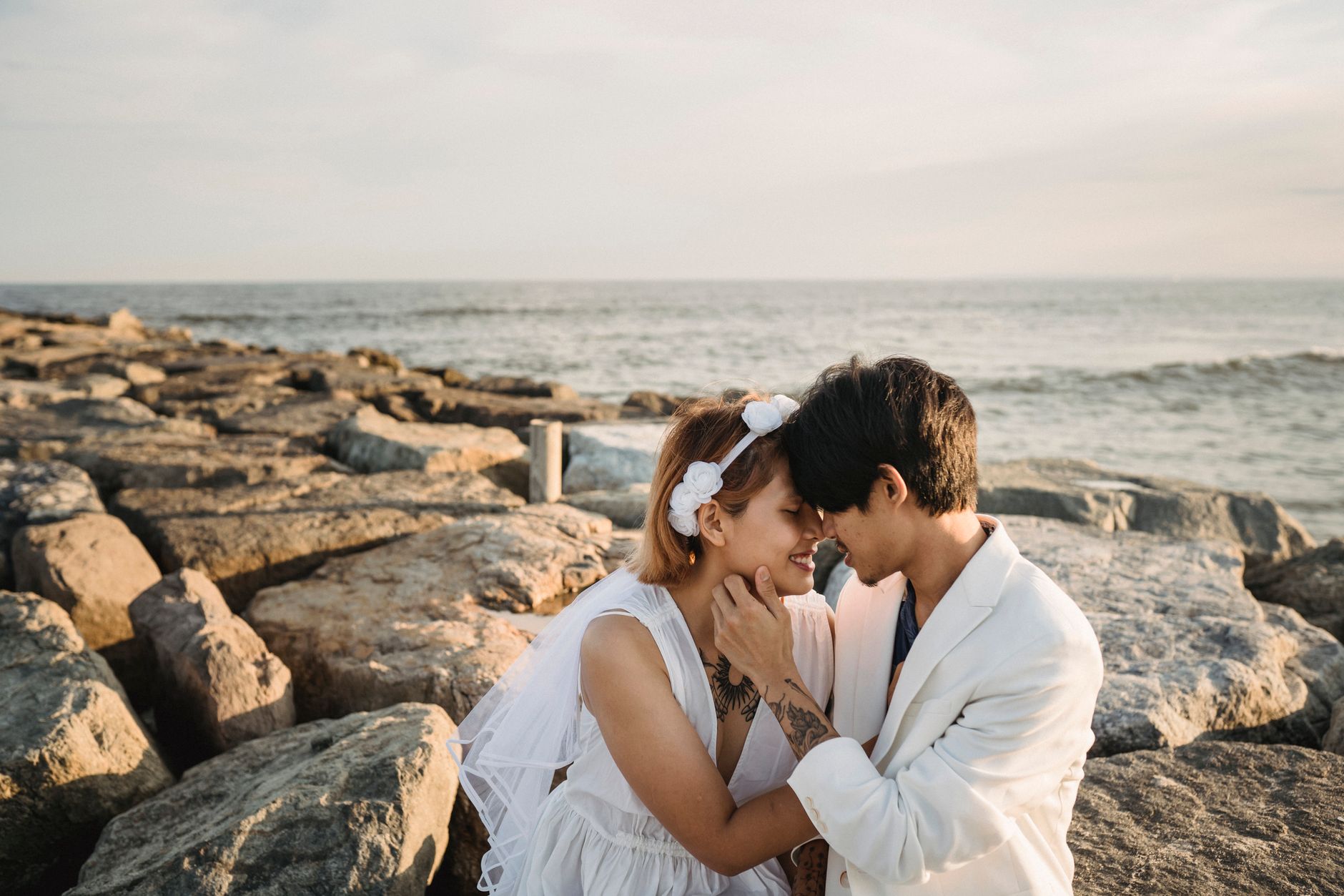A couple sharing an intimate moment on rocky beach by the sea at sunset.
