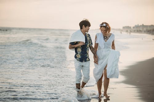 Free Couple Walking on the Shore while Holding Hands Stock Photo