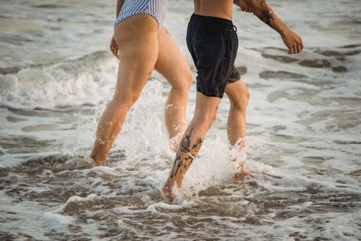 A man and woman enjoy a walk along the beach, feeling the ocean waves on their legs.