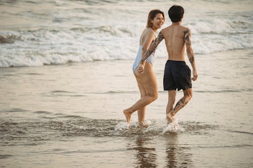 Free Man and Woman in their Swimwear Walking on the Beach Stock Photo