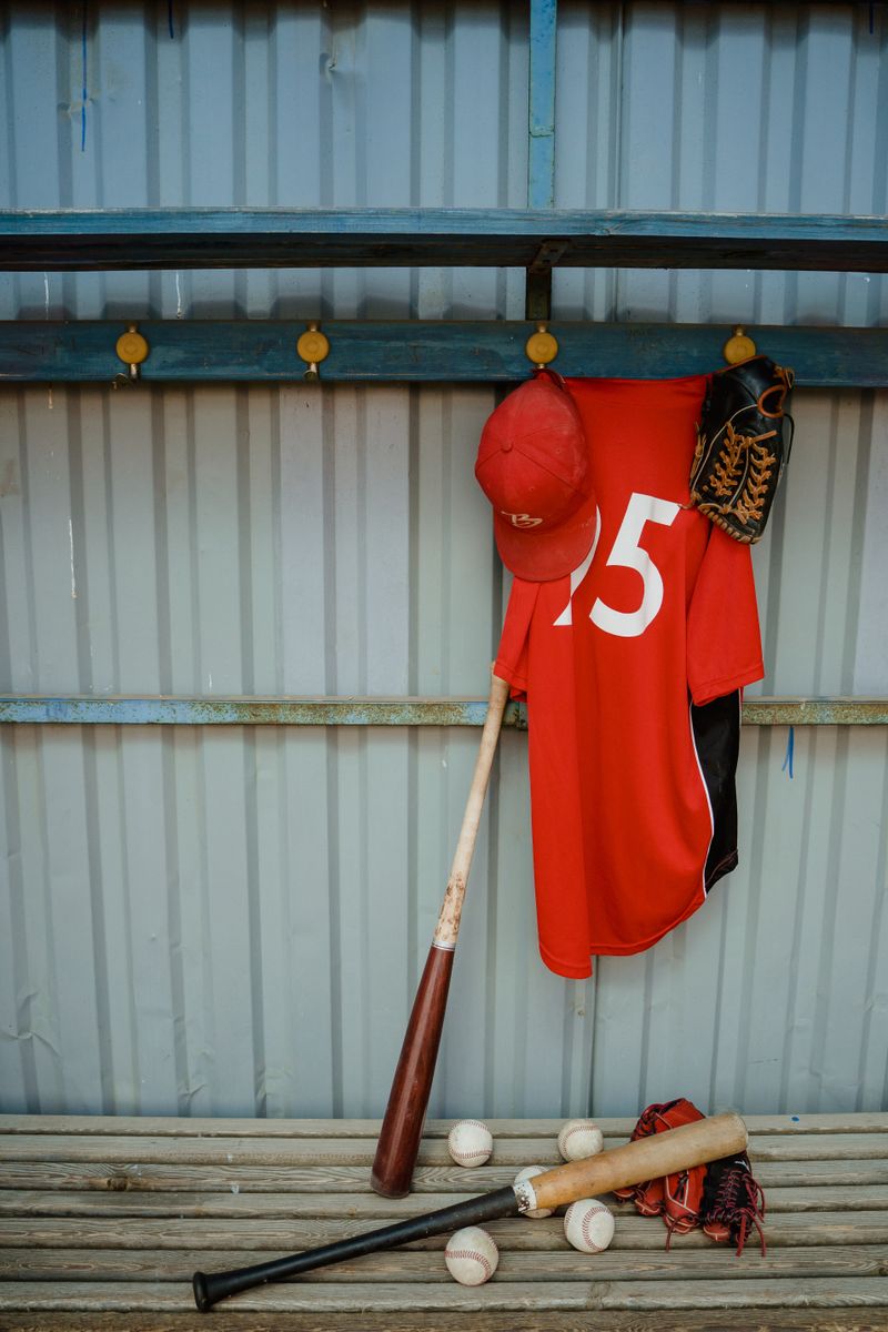 Red baseball jersey and bat hanging in a dugout