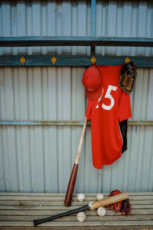 Free Red jersey and baseball gear hanging in dugout awaiting game day. Stock Photo