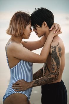 A couple in swimwear shares an intimate moment on a sandy beach, exuding love and connection.