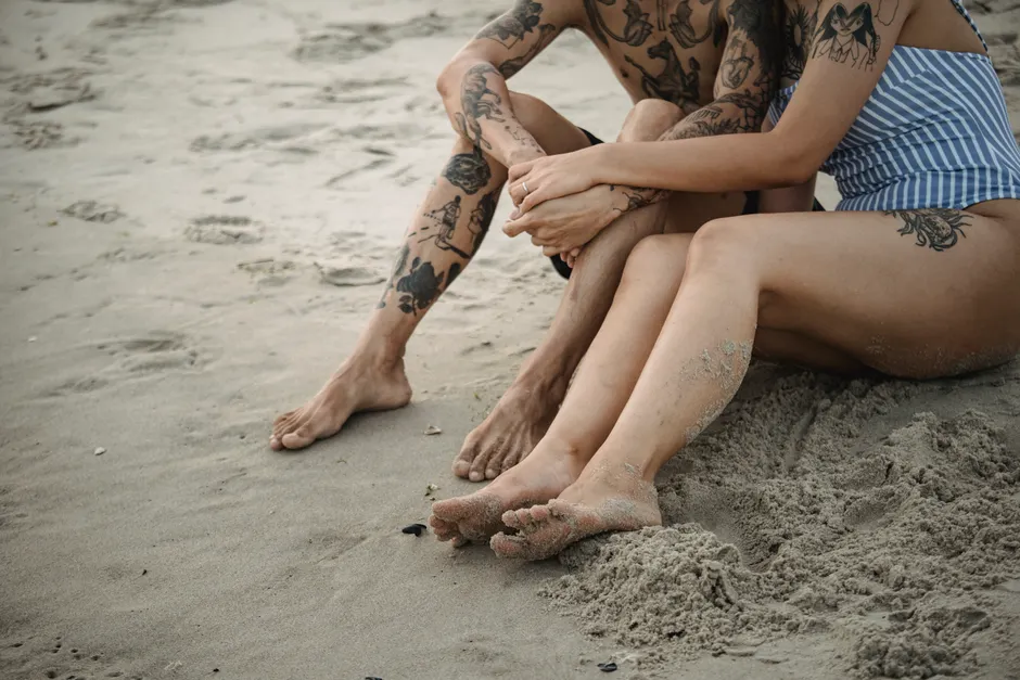 Couple at beach displaying temporary tattoos on shoulders and legs, stylish casual look