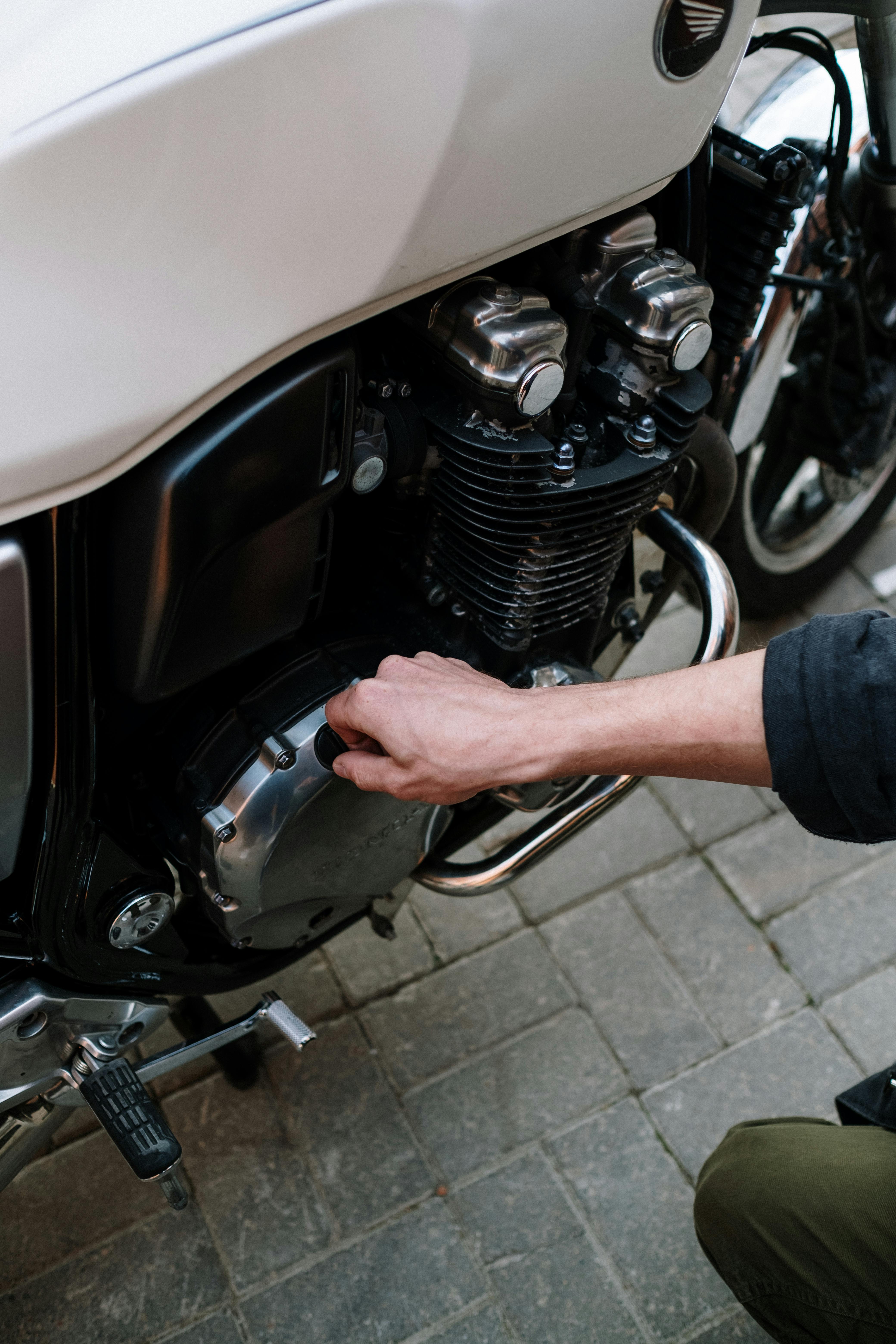 Close-up of a person working on a motorcycle engine outdoors.