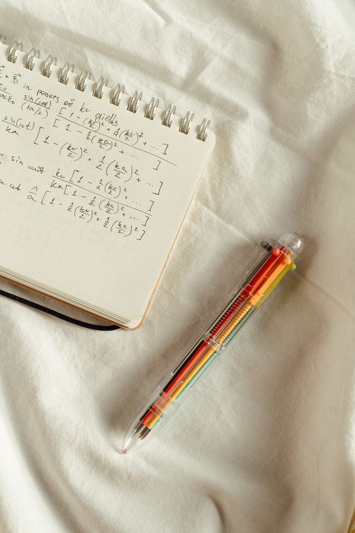 Handwritten mathematical formulas in a study notebook with a pen