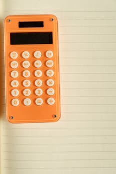 An orange calculator resting on a lined notebook providing education or business visuals with ample copy space.