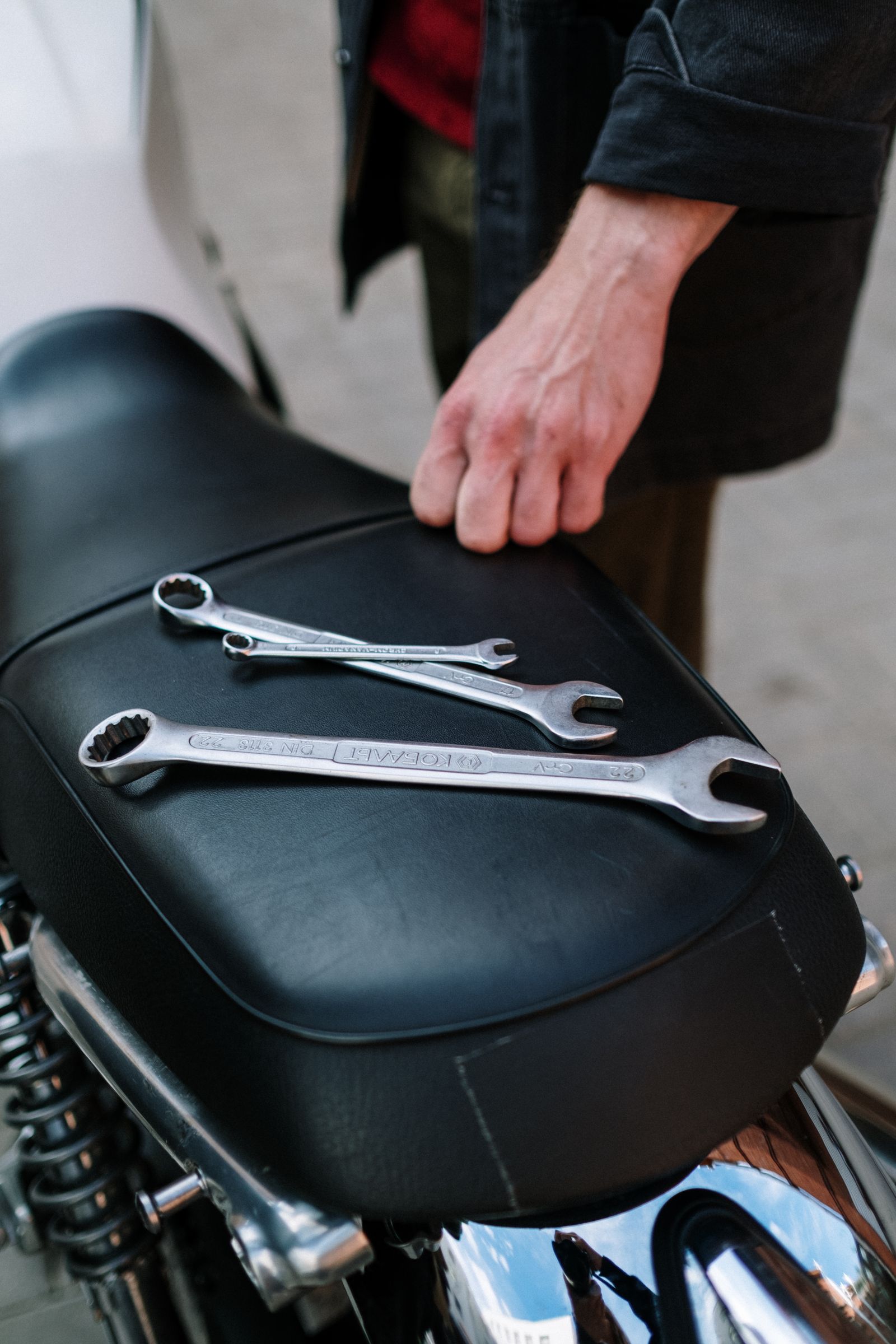 Main d'un mécanicien tenant des clés posées sur la selle d'une moto