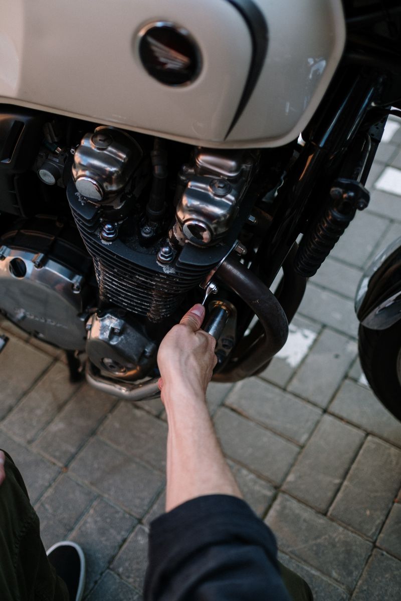 Close-up of a mechanic's hand fixing a motorcycle engine outdoors.