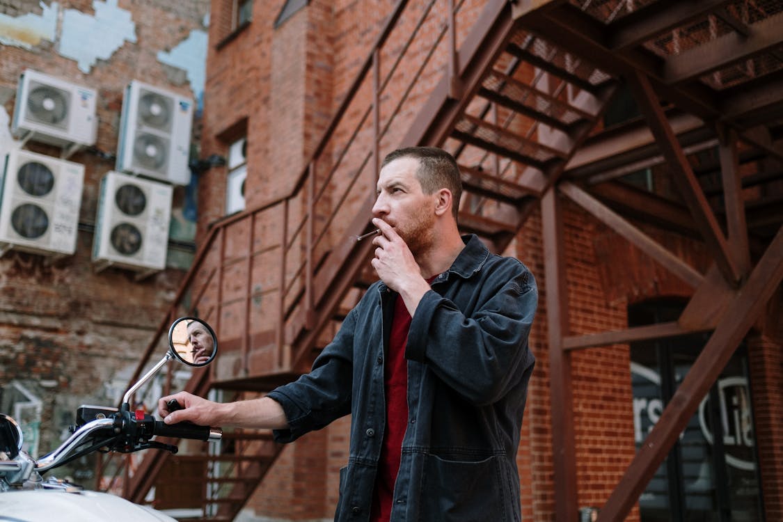 https://www.pexels.com/photo/man-in-black-jacket-smoking-beside-motorcycle-in-front-of-brick-building-5184994/