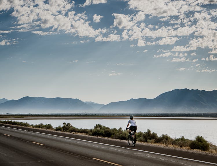 Man On Bike Riding Empty Road Near Lake