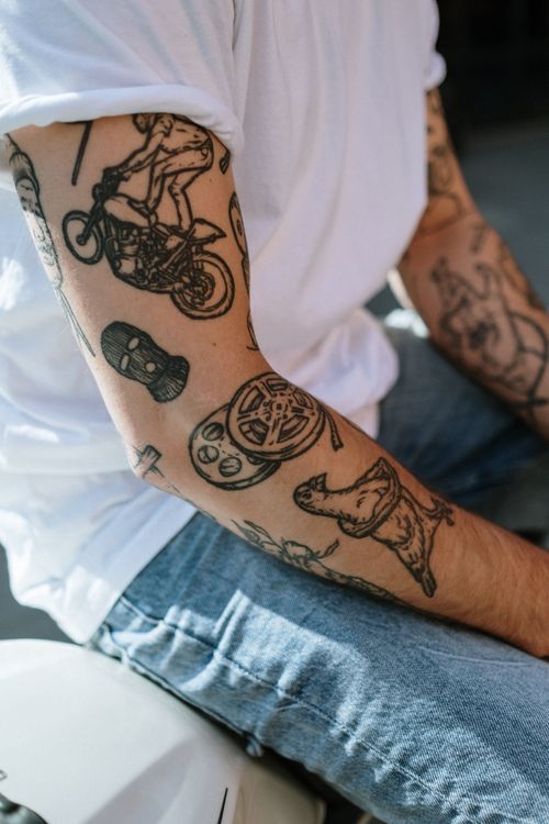 Free A detailed shot of a tattooed arm wearing a white shirt and denim pants, showcasing unique designs. Stock Photo