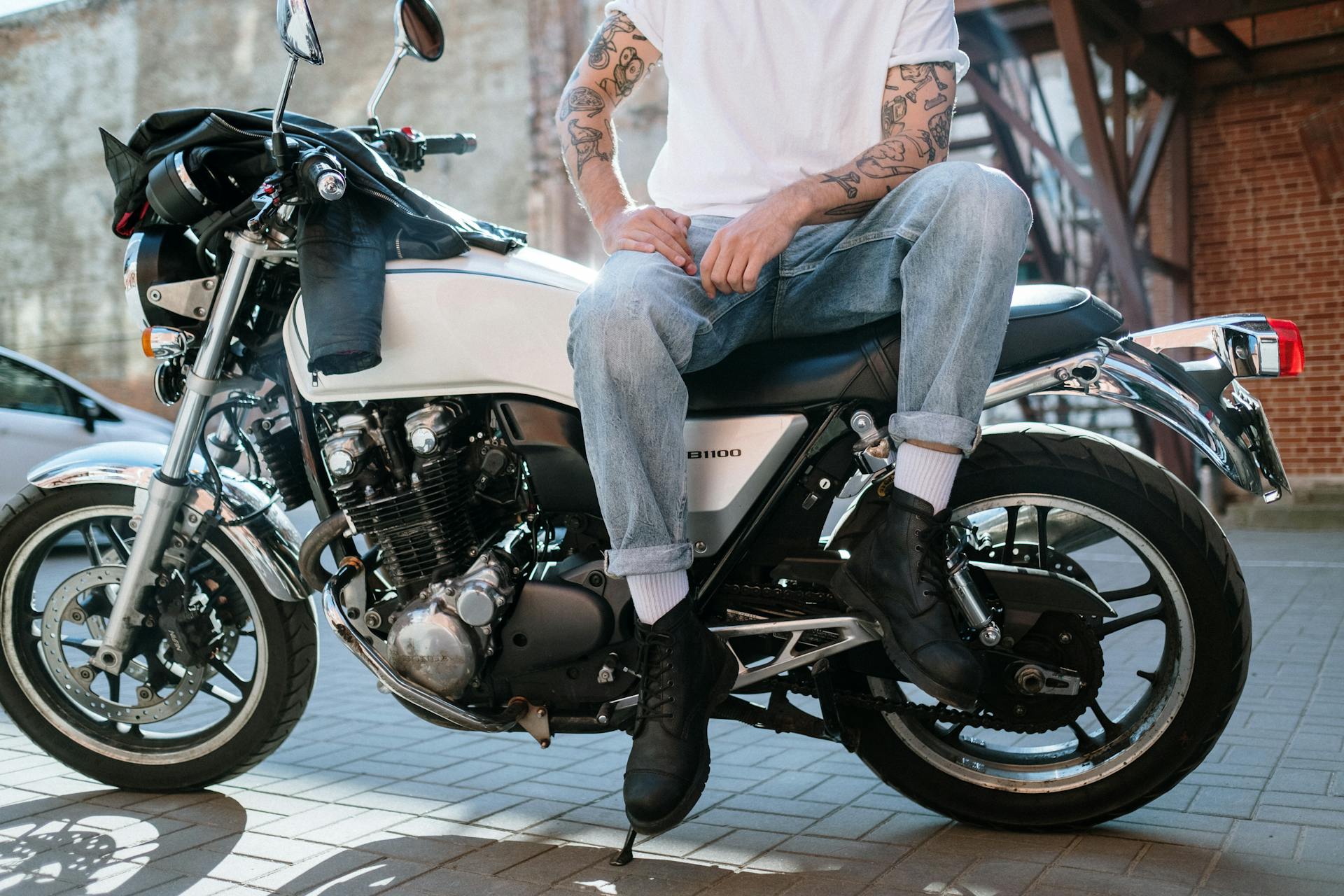 Casual biker with tattoos sitting on a motorcycle in an urban setting.