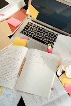Messy creative workspace with open laptop, notebooks, and sticky notes.