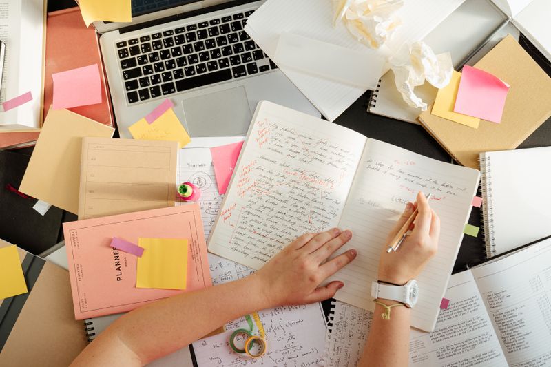 Person organizing notes and study materials on a desk with a laptop