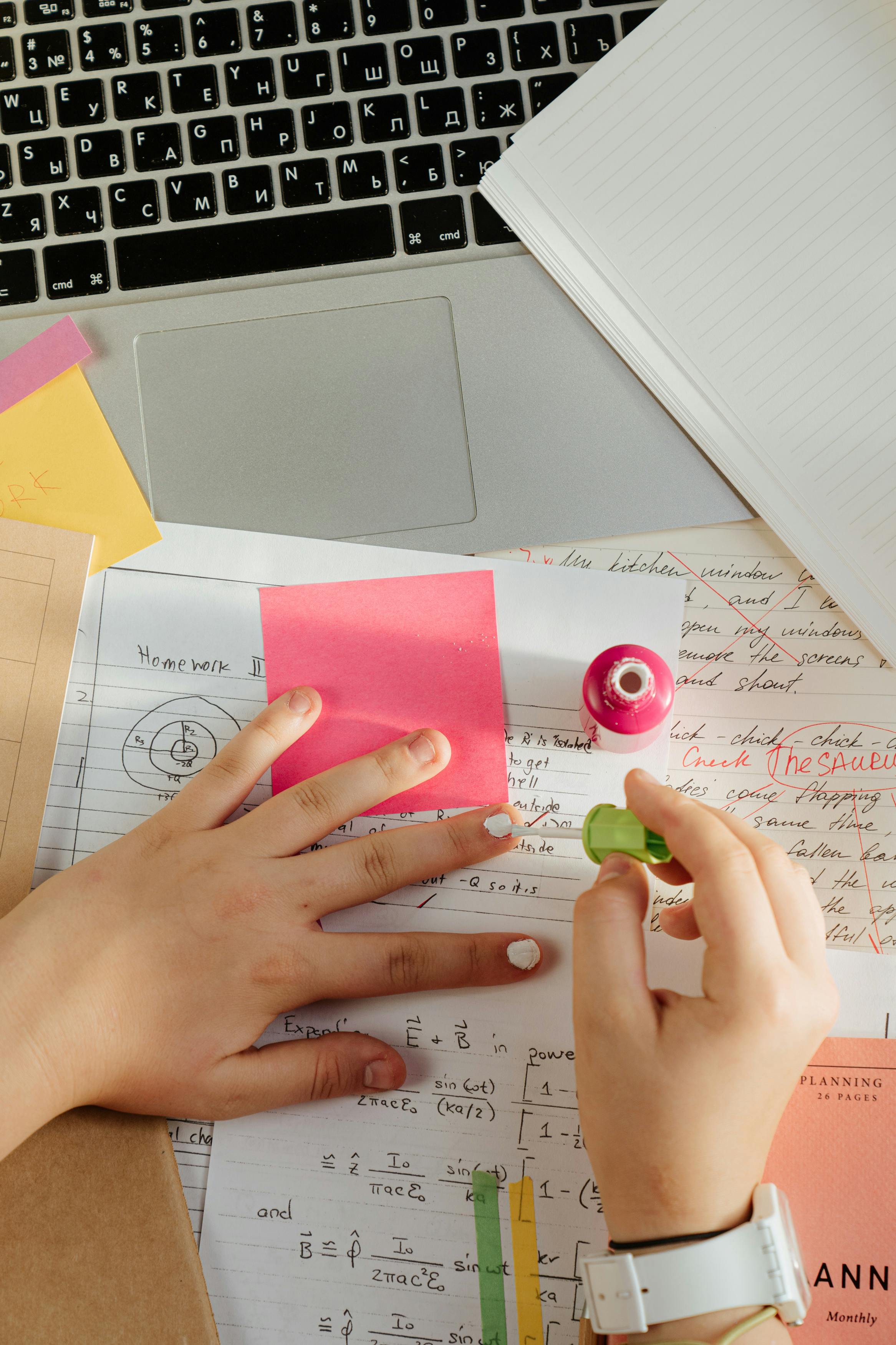 一个人涂着指甲油，一只手操作笔记本电脑，周围散落着学习笔记