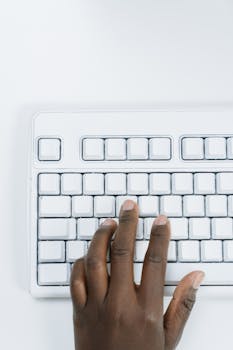 A hand typing on a white keyboard on a clean surface.