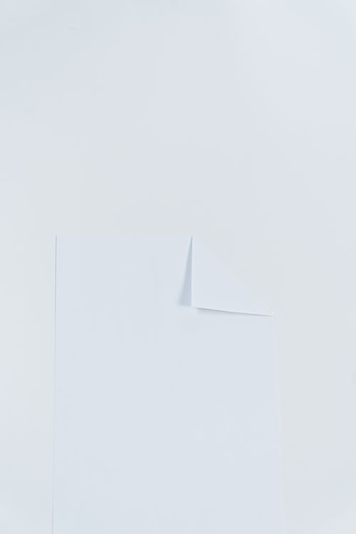Free A simple sheet of white paper with a folded corner on a plain light background, perfect for design projects. Stock Photo
