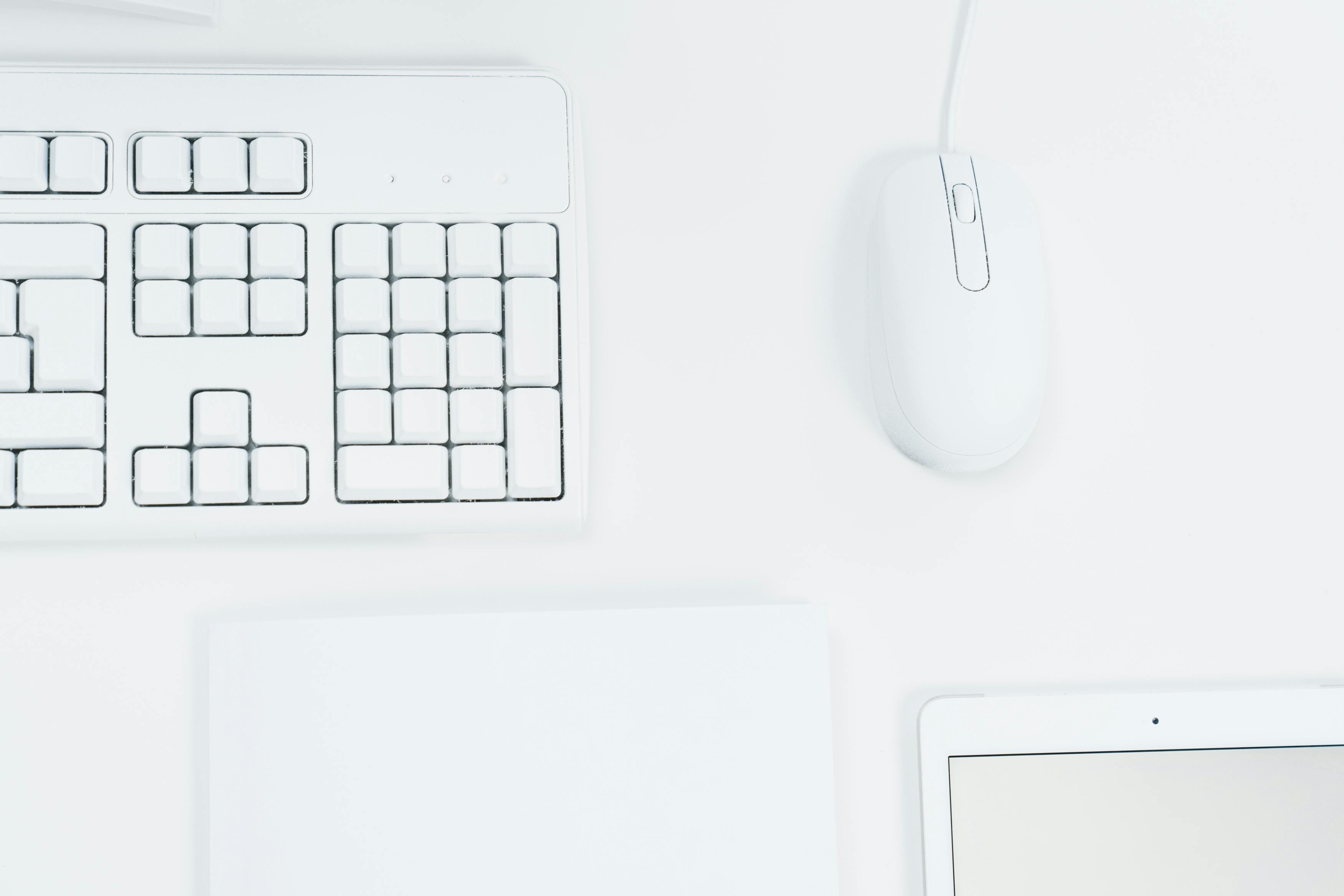 Clean, minimalist white workspace featuring a keyboard, mouse, and tablet.