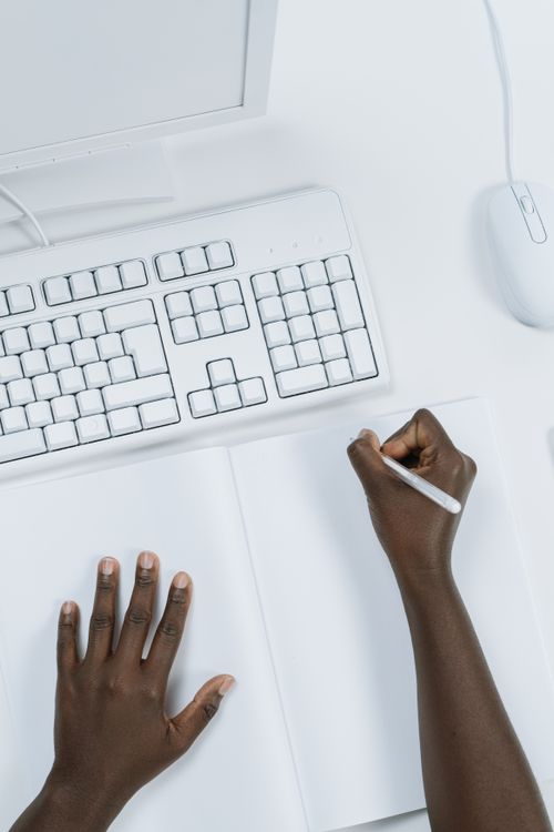 Person Writing on a Notebook In Front of a Computer · Free Stock Photo