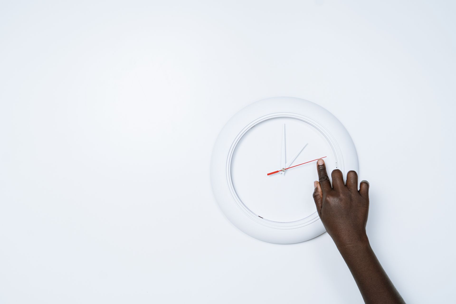 Close-up of a hand adjusting a modern white wall clock on a minimalist background.