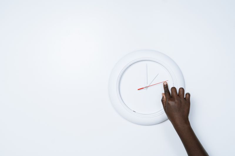 Mano ajustando un reloj de pared que marca la ventana horaria de comidas del ayuno intermitente