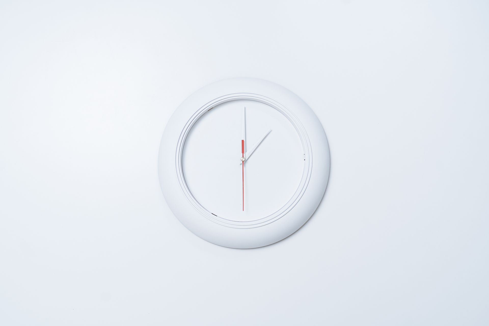 Simple minimalist wall clock with red and white hands on a light background.