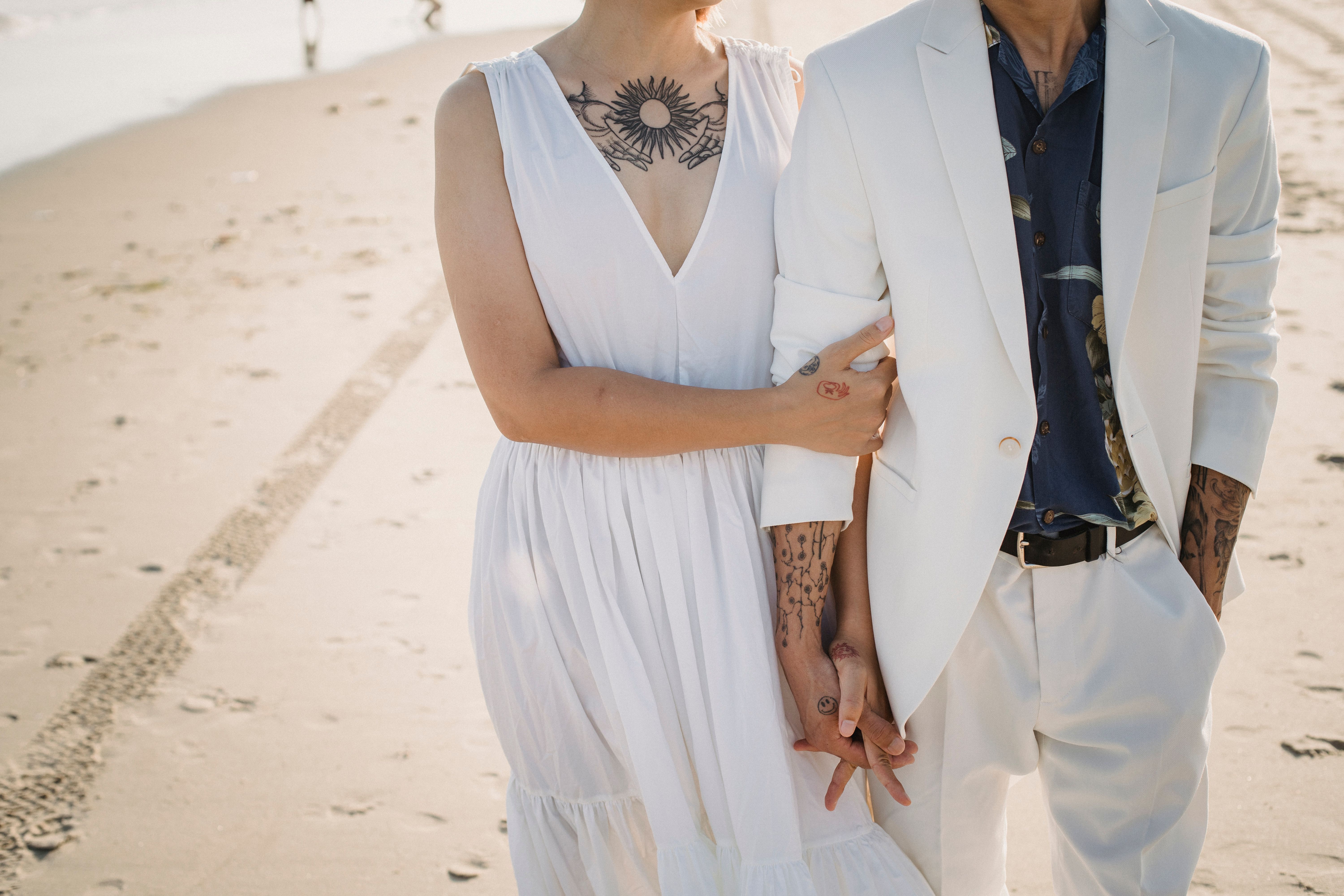Jeunes mariés main dans la main sur la plage, alliances et style naturel tatoué