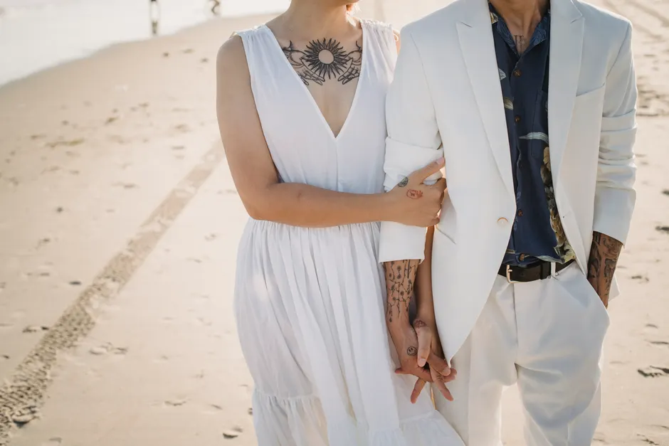 Jeunes mariés main dans la main sur la plage, alliances et style naturel tatoué