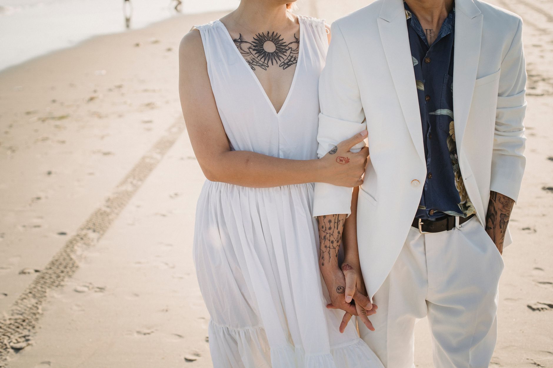 Jeunes mariés main dans la main sur la plage, alliances et style naturel tatoué