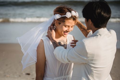 Free A couple sharing a tender moment on the beach in wedding attire, enveloped in warmth. Stock Photo